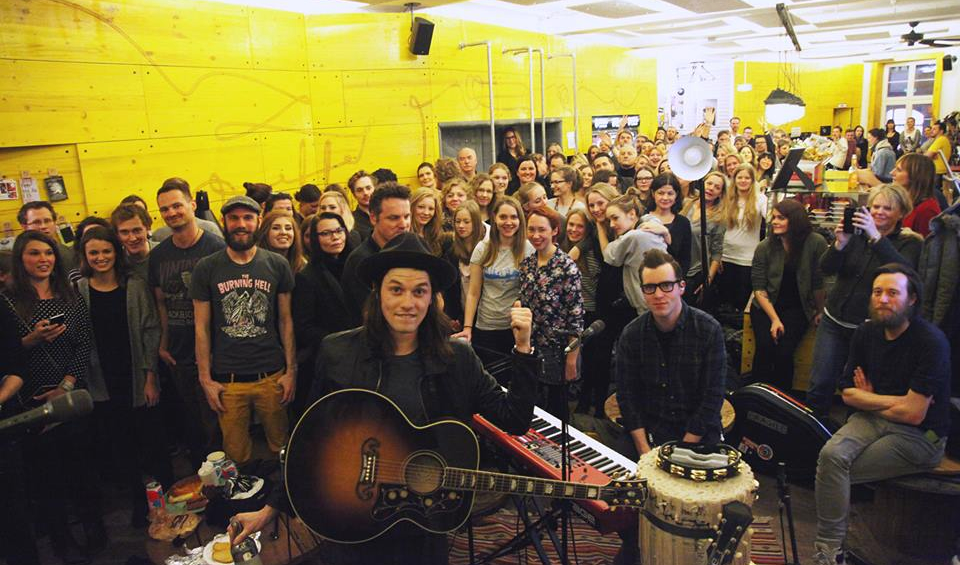 Ein großes Publikum  steht hinter einer Band und guckt in die Kamera.